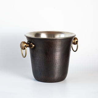 Handmade hammered copper ice bucket with a dark oxidized finish, solid brass ring handles, and tin-lined interior, ideal for chilling wine or spirits.